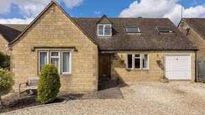 A two-story house with a stone facade, a front door, a small porch, and a gravel driveway. - Central Bourton Gem|5 Bedrooms|Garden|Parking - Pass the Keys (Bourton-on-the-Water)