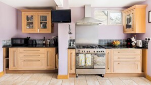 A kitchen with wooden cabinets, a gas stove, a microwave, and a television. - Central Bourton Gem|5 Bedrooms|Garden|Parking - Pass the Keys (Bourton-on-the-Water)