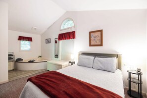 Un dormitorio con cama, ventana con cortinas, bañera, una mesita y un cuadro colgado en la pared.