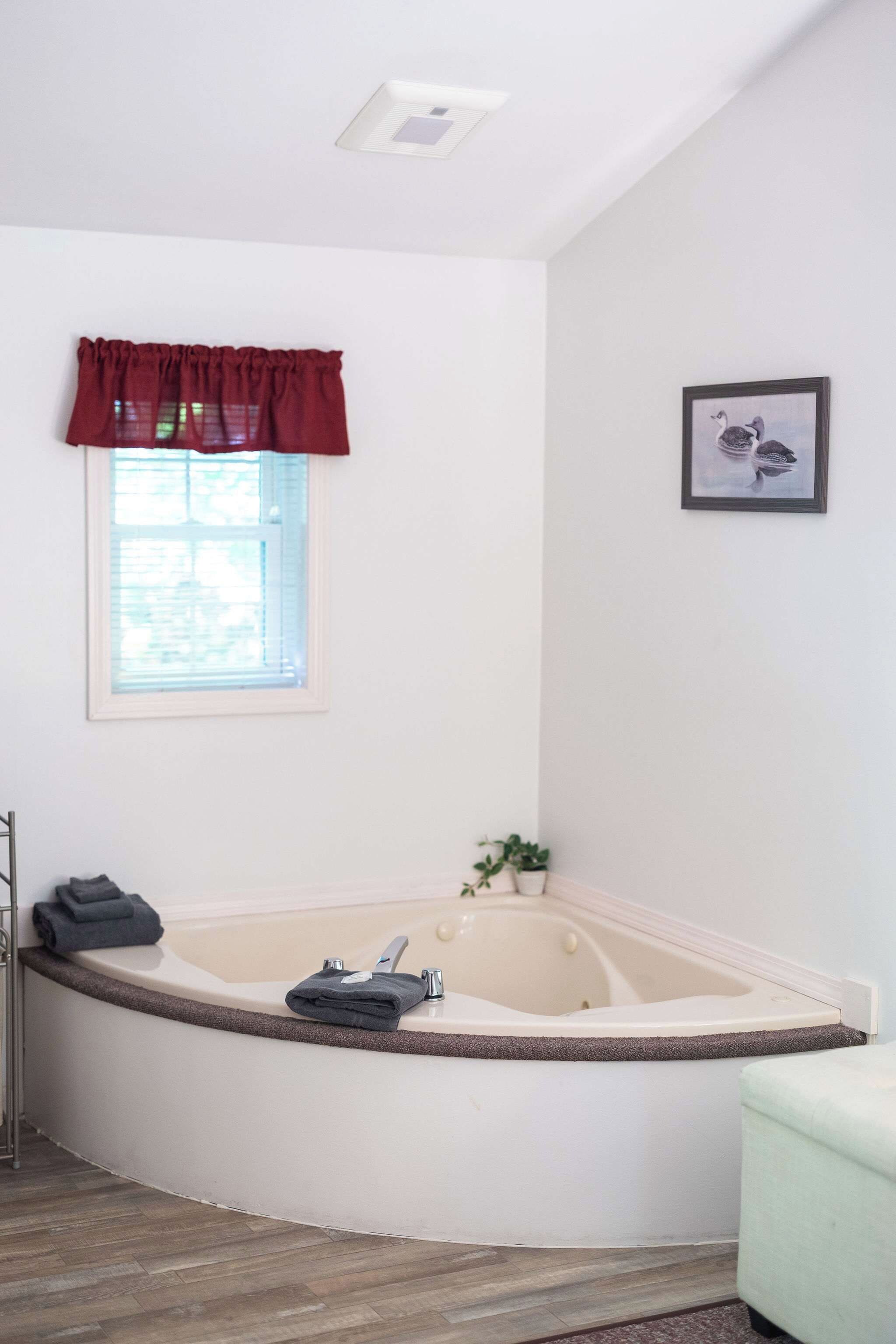 A bathroom with a freestanding bathtub, a window with a red valance, and a framed picture on the wall.