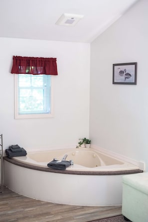 A bathroom with a freestanding bathtub, a window with a red valance, and a framed picture on the wall.