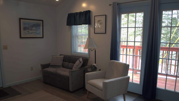 A living room with a sofa, armchair, window with blinds, and a lamp. - Little Acorn Landing (Norway)