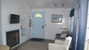 A living room with a fireplace, a blue door, a television mounted on the wall, a sofa, and a lamp. - Little Acorn Landing (Norway)