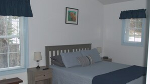 A bedroom with a bed, nightstands, a lamp, a picture on the wall, and a window with blinds. - Little Acorn Landing (Norway)
