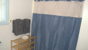 A bathroom with a shower curtain, a towel rack with towels, and a wooden shelf with a bowl. - Little Acorn Landing (Norway)