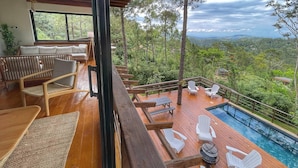 A wooden deck with outdoor seating, a pool, and a scenic view of a forested landscape. - Escápate al Bosque · Villa Completa · Piscina · BBQ · Hasta 12 Huéspedes (Jarabacoa)