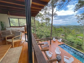 A wooden deck with outdoor seating, a pool, and a view of a forested landscape.