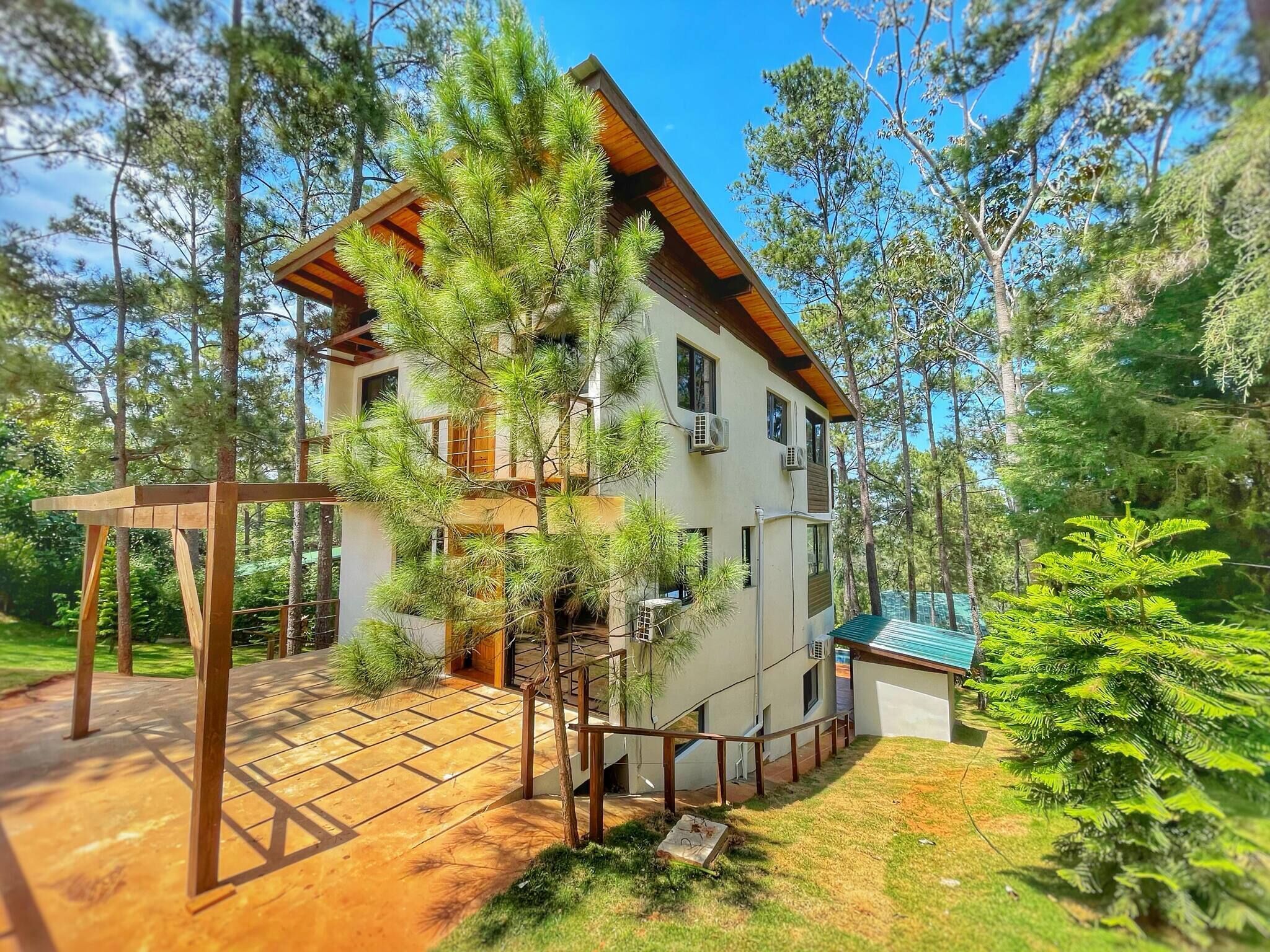 A two-story house with a wooden deck, surrounded by trees.