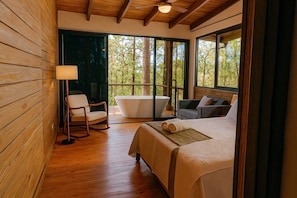 A wooden cabin with a bed, a chair, a bathtub, and large windows.