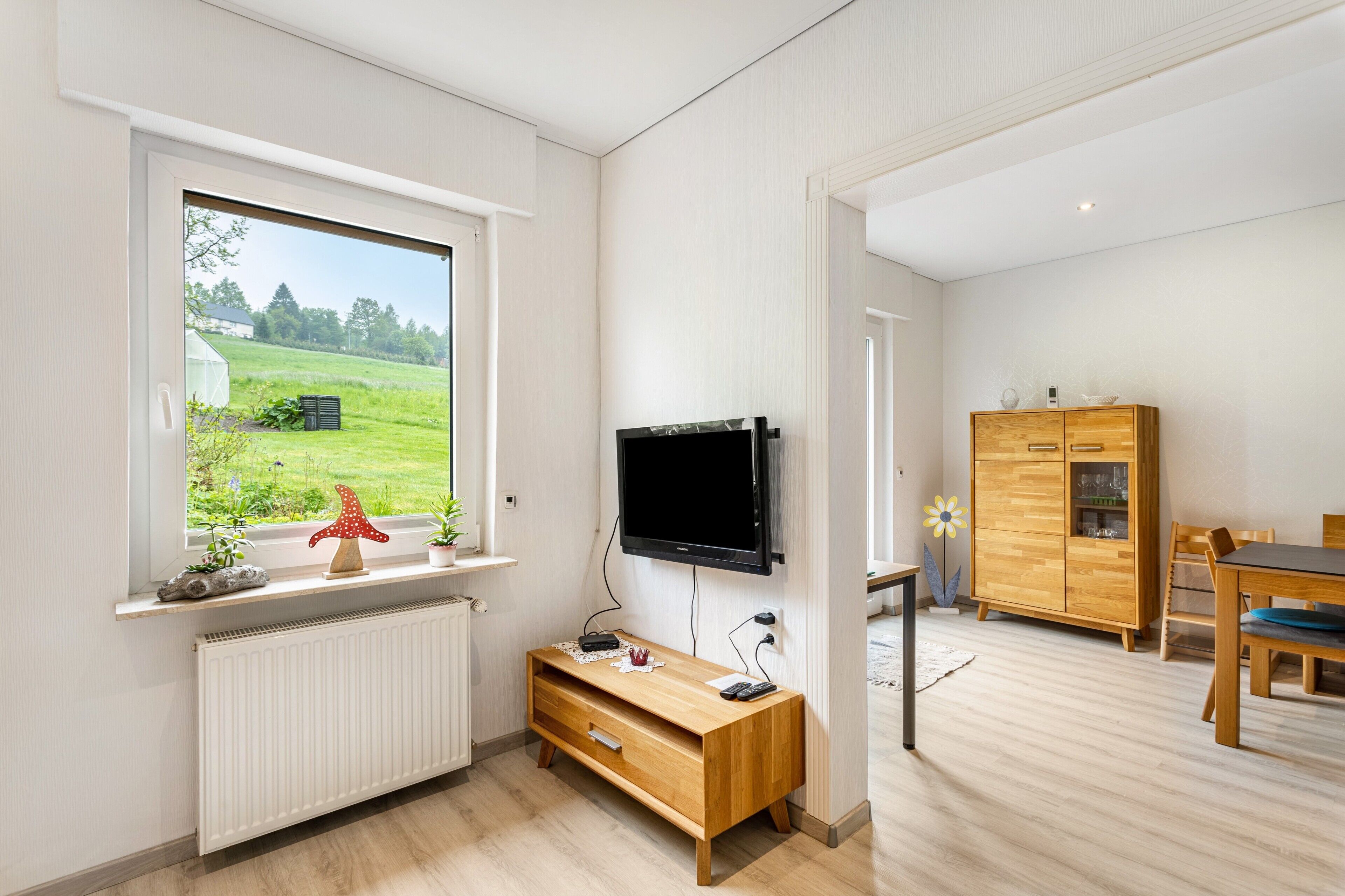 Ein modernes Wohnzimmer mit Fernseher, einer Holzunterhaltungsecke und Blick auf ein grünes Feld.