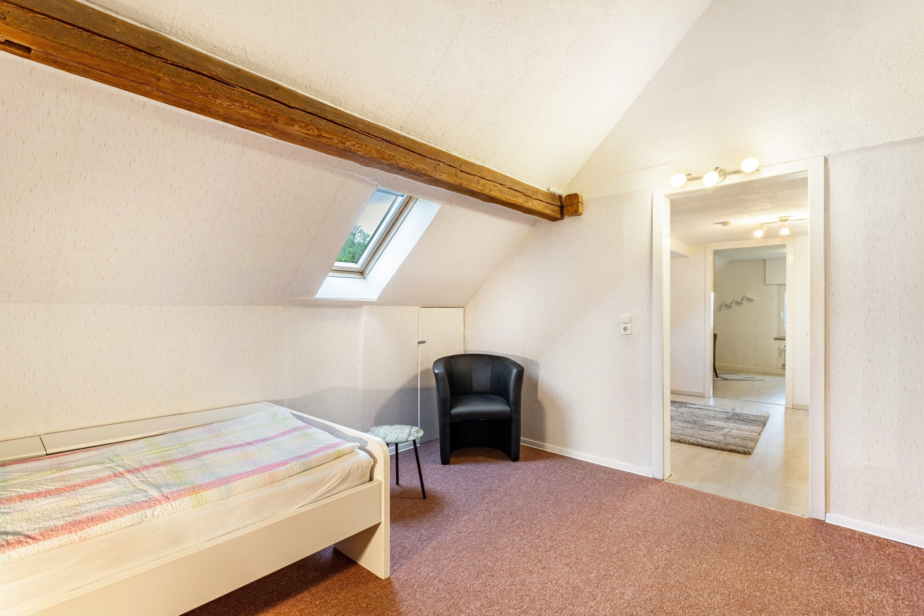 Une chambre à coucher comprenant un lit, une chaise, une petite table, une lucarne et un miroir.