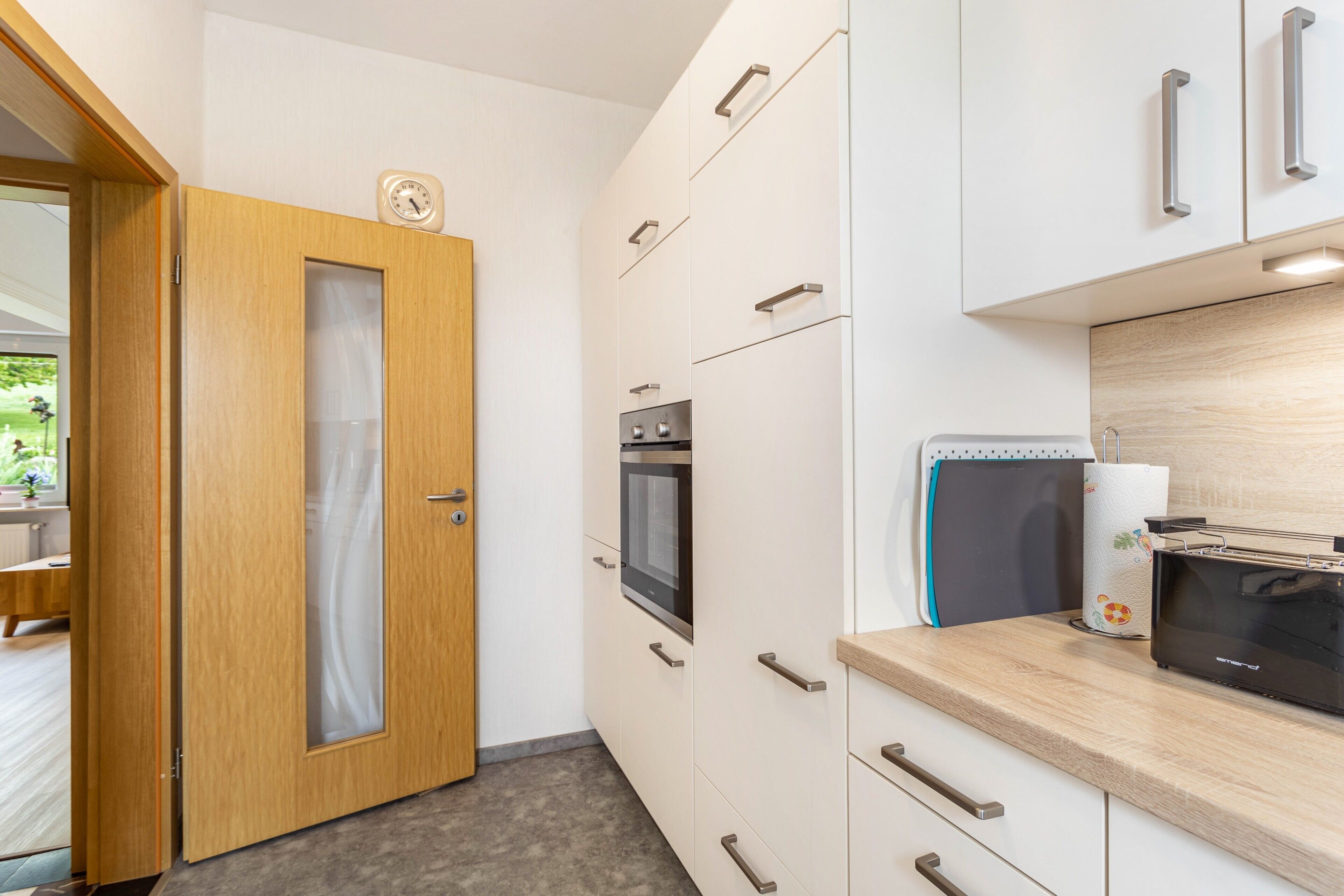 Una cocina moderna con armarios blancos, una puerta de madera, un microondas y un tostador.
