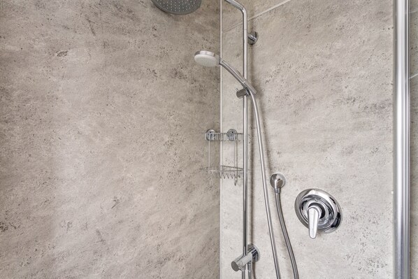 A shower with a handheld showerhead, a wall-mounted faucet, and a control knob.