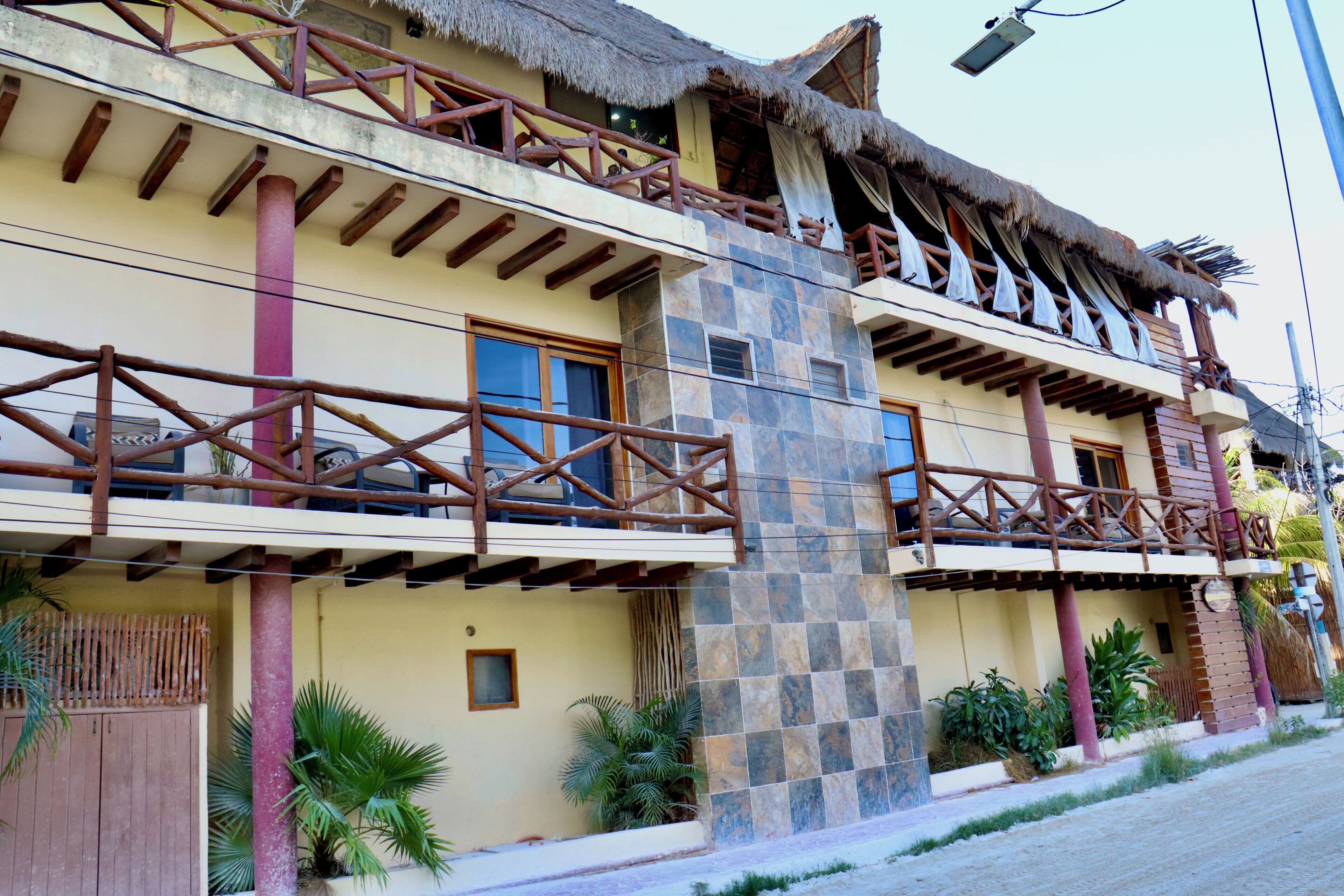 Un edificio de dos pisos con un balcón, techo de paja y un pilar de piedra.