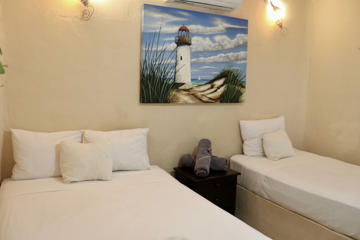 A hotel room with two beds, a painting of a lighthouse, and a nightstand with towels.