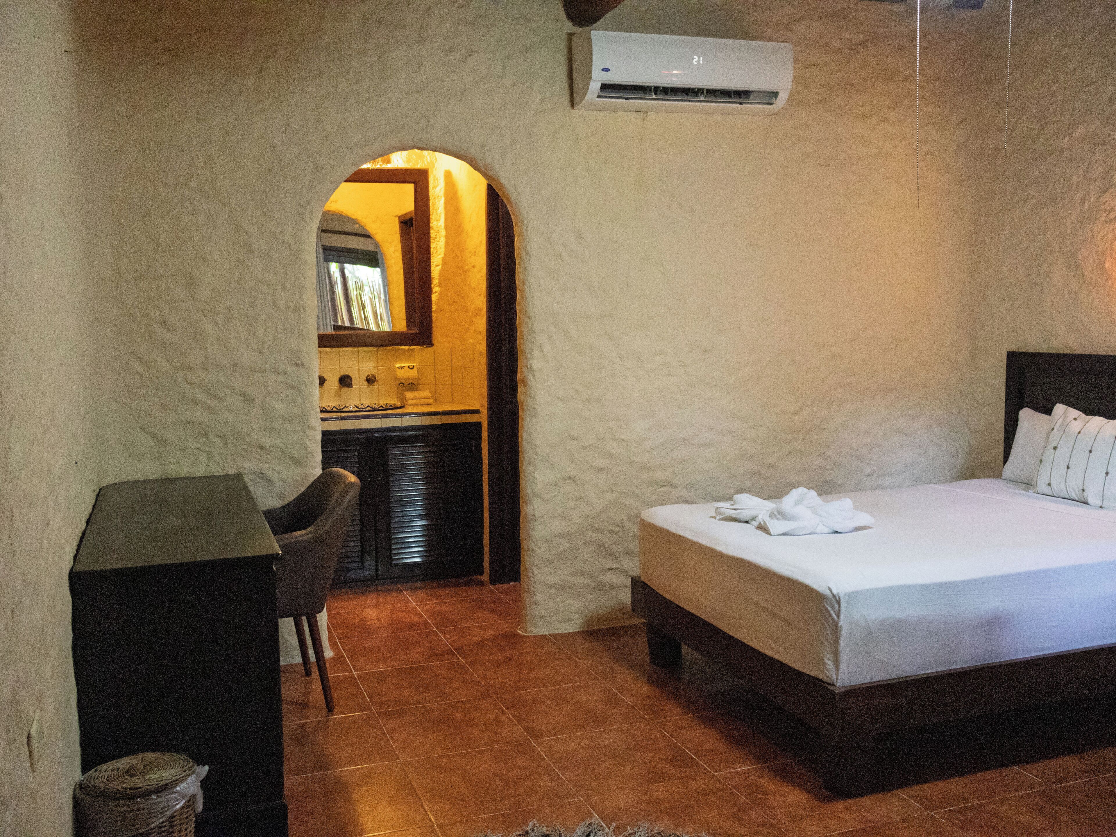Een slaapkamer met een bed, een bureau en een kitchenette op de achtergrond.