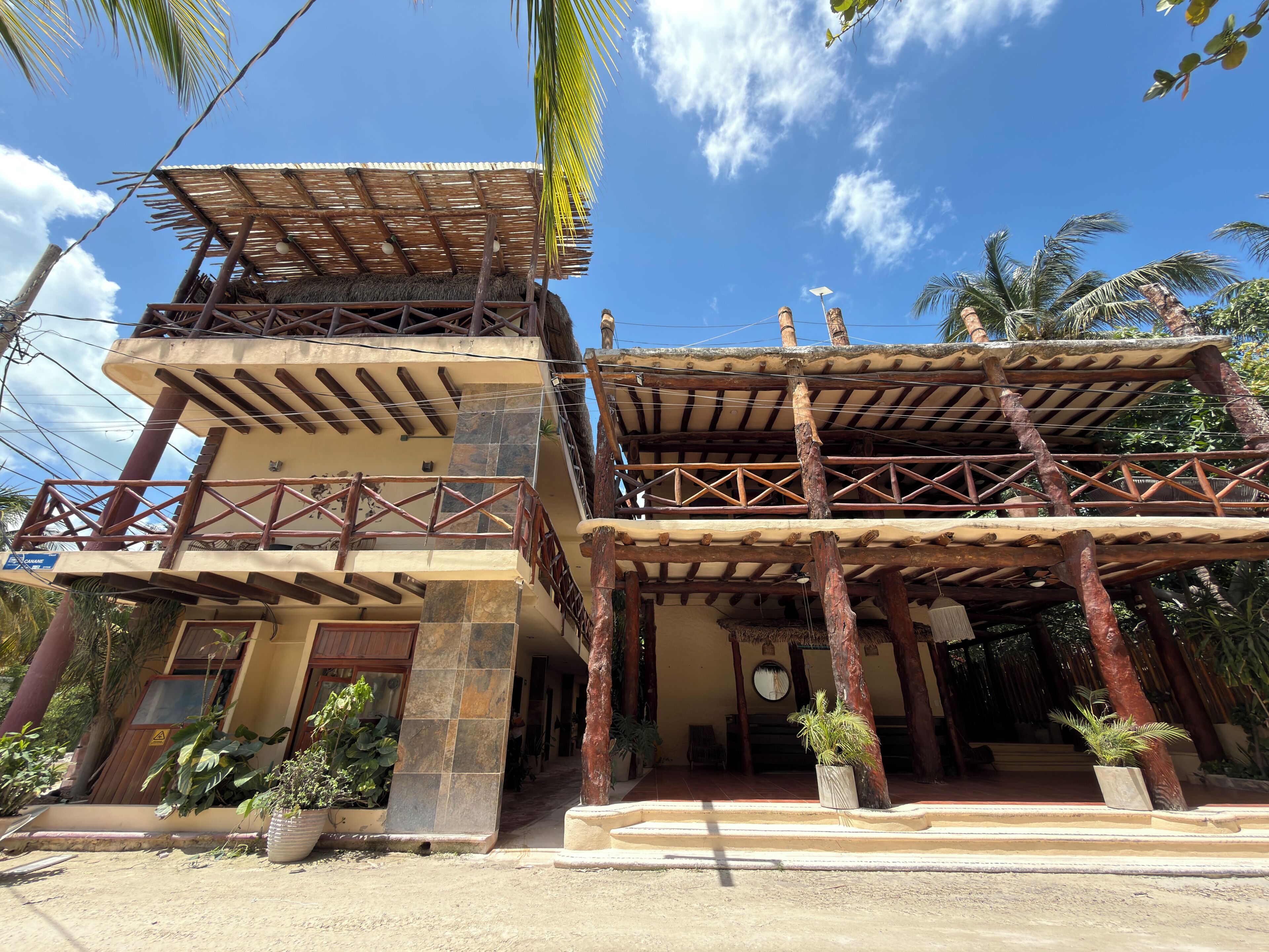 A multi-story building with a balcony, a thatched roof, and potted plants.