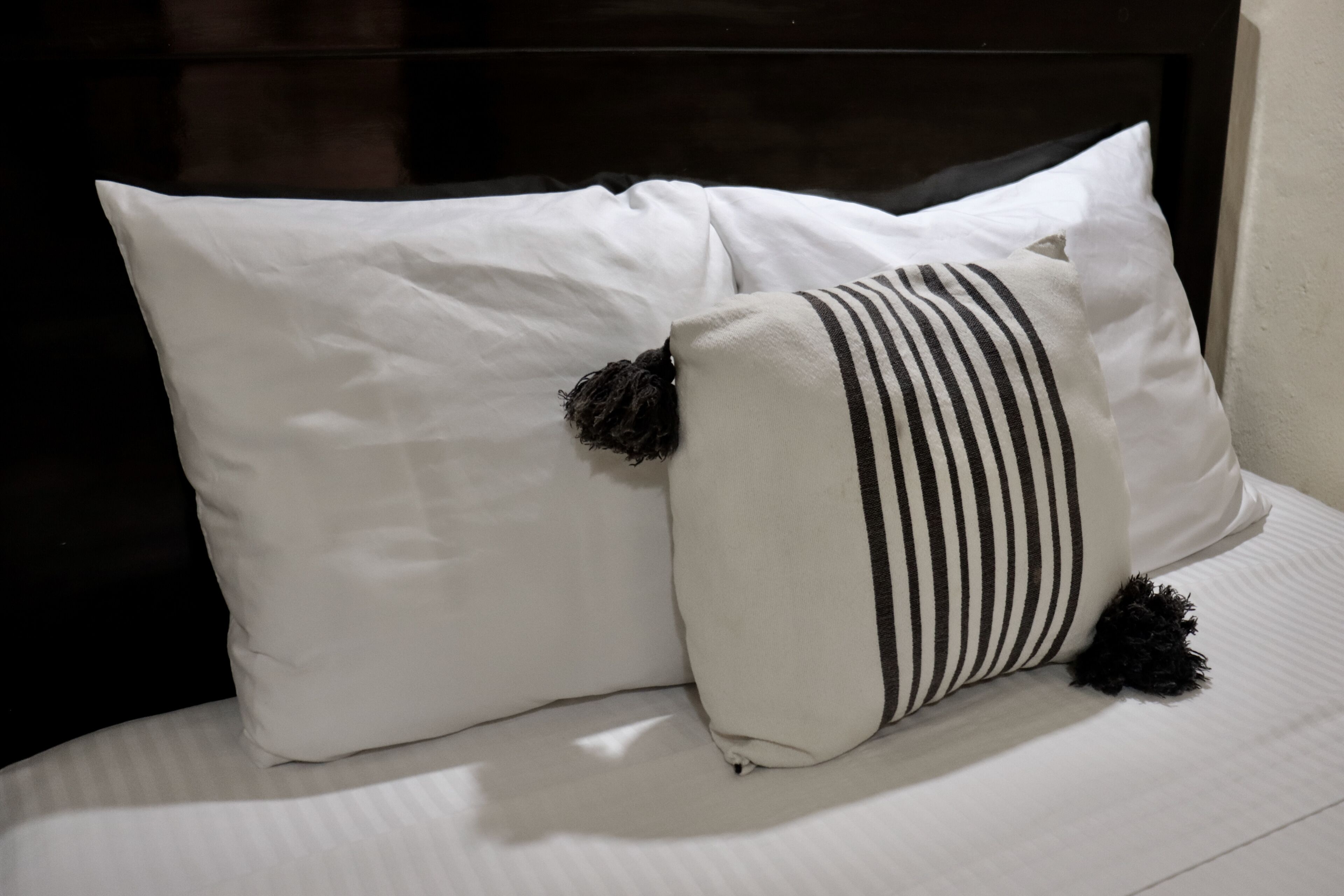 Una cama con ropa de cama blanca y dos almohadas, una a rayas y otra lisa.