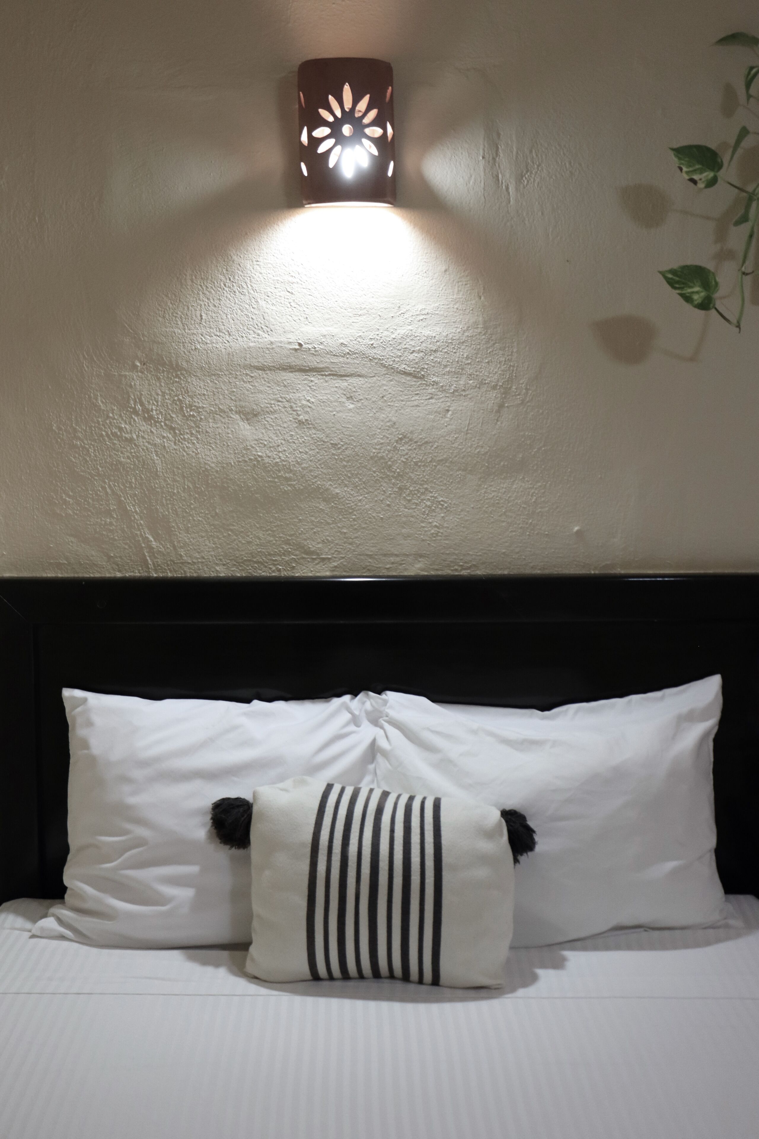 Un lit avec une literie blanche, une tête de lit noire et un luminaire fixé au mur.