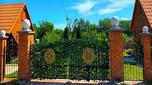 Une entrée fermée par un portail, précédée d’un mur en briques surmonté de deux éléments décoratifs sphériques, et un portail en métal orné de deux médaillons circulaires.
