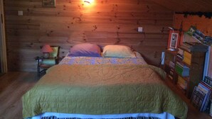 Une chambre confortable, aménagée dans un chalet en bois, avec un lit, des oreillers, une table de chevet et une bibliothèque.