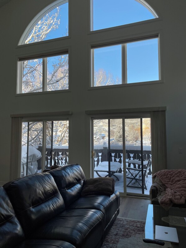 Ein Wohnzimmer mit einer Ledersofa, einem Glastisch und Blick durch große Fenster auf eine verschneite Terrasse.