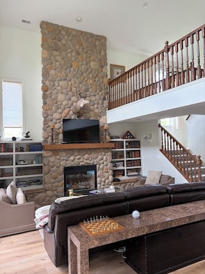Ein Wohnzimmer mit Kamin aus Stein, einem Flachbildfernseher, einem Bücherregal, einer Treppe und einem Ledersofa.