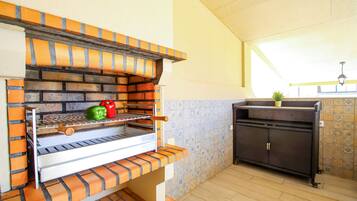 A brick oven with a shelf for cooking vegetables, a small cabinet, and a tiled backsplash.