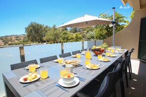 Un espace de restauration en plein air avec une longue table dressée pour le petit-déjeuner, entourée de chaises, et offrant une vue sur le paysage.