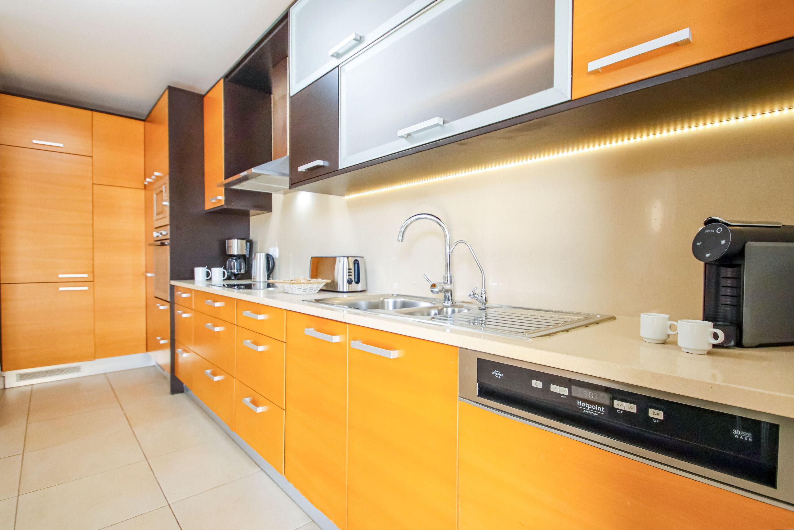 A modern kitchen with orange cabinetry, a stainless steel sink, and a dishwasher.