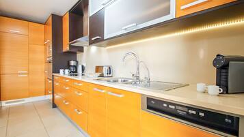 A modern kitchen with orange cabinetry, a stainless steel sink, and a dishwasher.