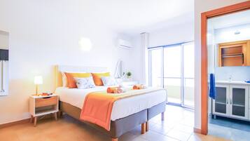 A hotel room with a bed, bedside table, lamp, and a view of the outside.