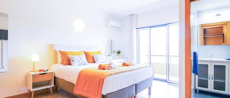 A hotel room with a bed, bedside table, lamp, and a view of the outside.