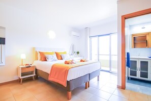 A hotel room with a bed, bedside table, lamp, and a view of the outside.