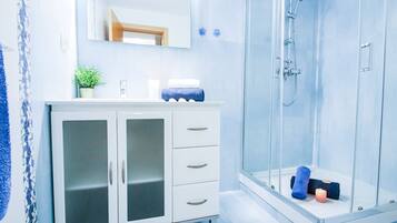A modern bathroom with a glass shower enclosure, a white vanity with a mirror, and a potted plant.