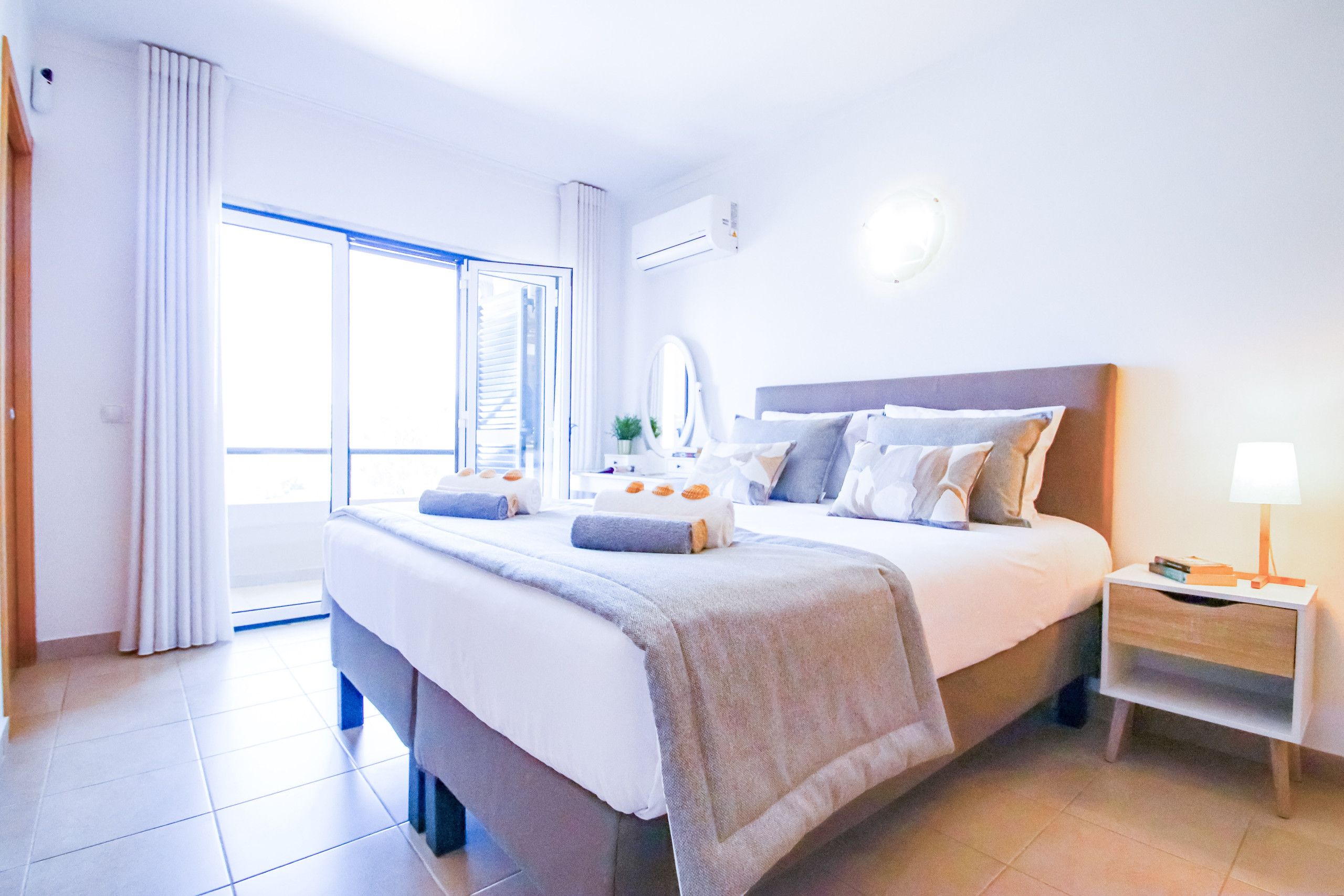 Habitación de hotel con una cama grande, una mesita de noche, una lámpara y vistas al exterior.