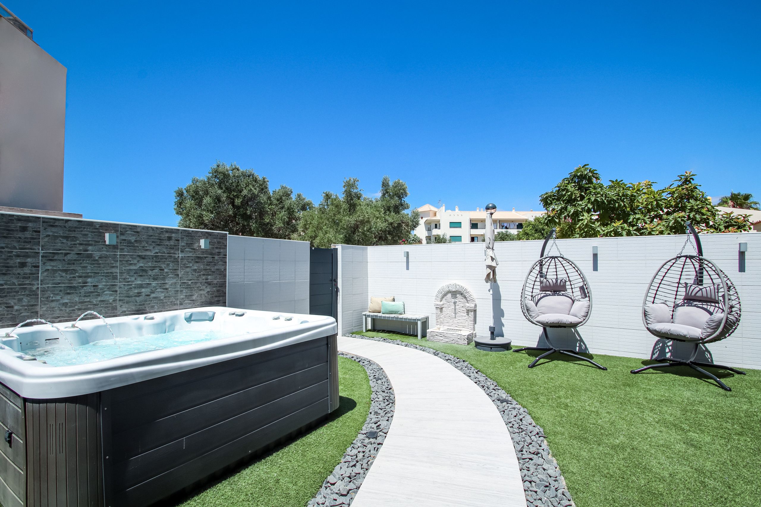 A backyard with a hot tub, two egg chairs, a stone bench, and a stone wall.