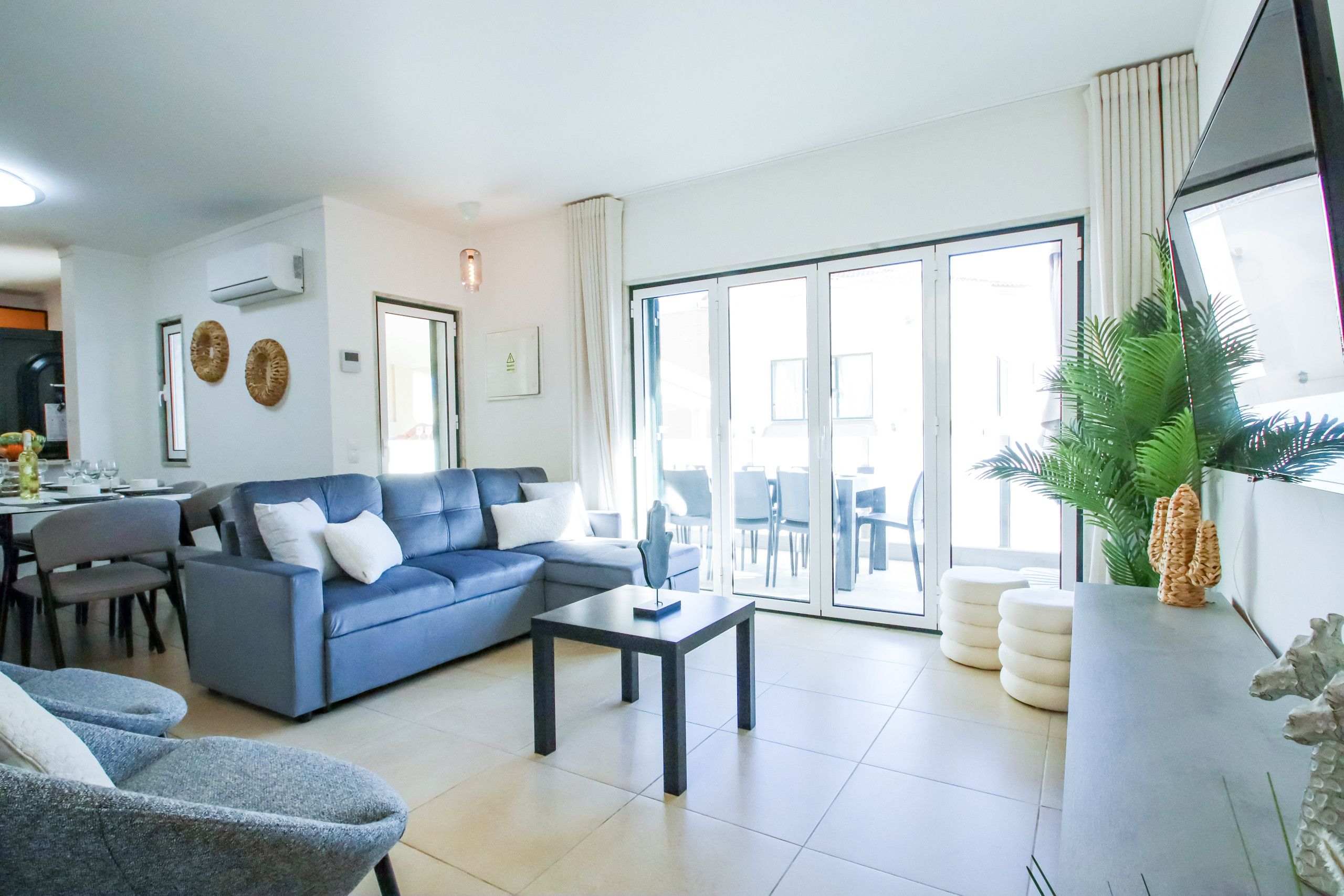A modern living room with a blue sofa, a coffee table, and a dining area with chairs.
