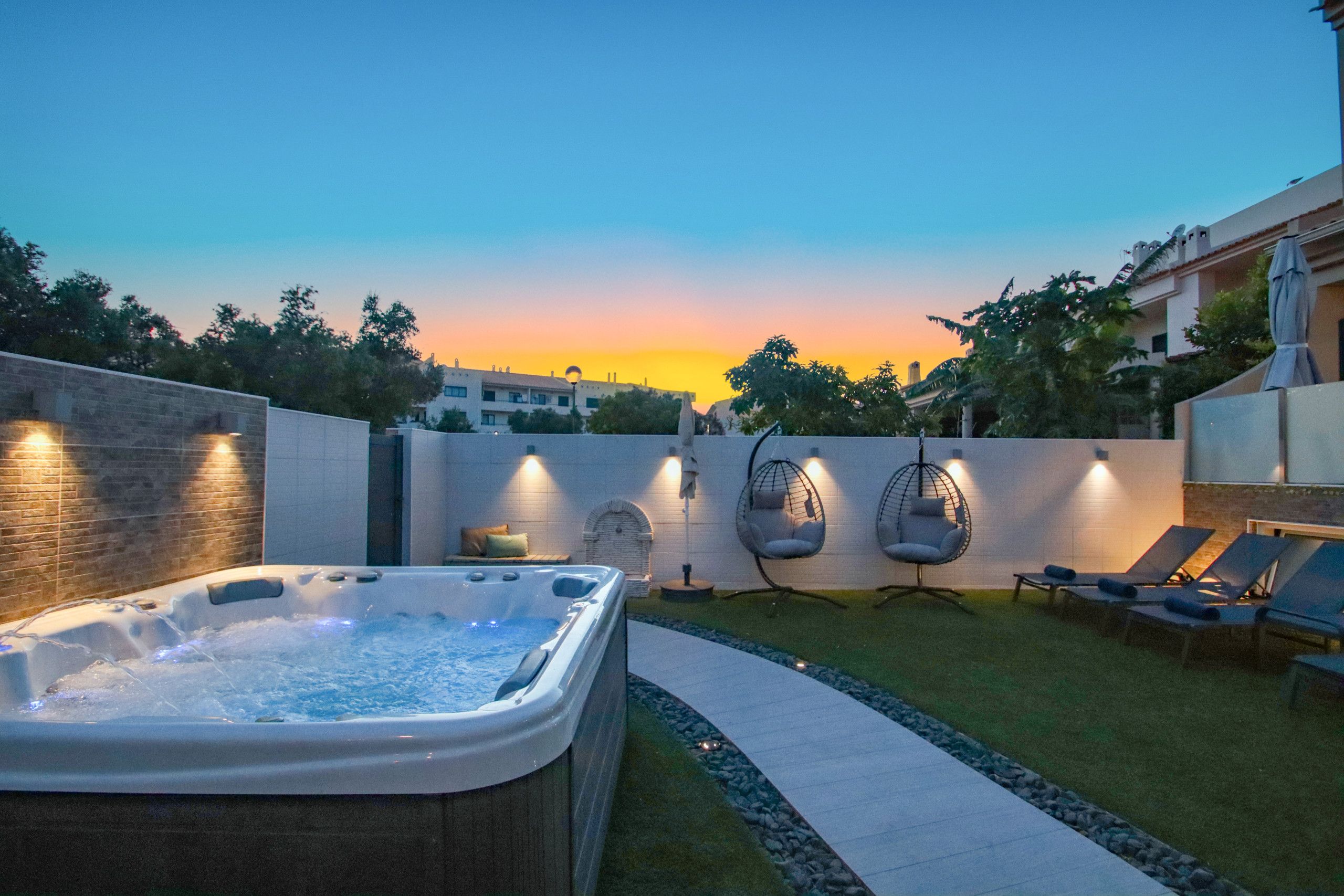 A hot tub, lounge chairs, and a sunset view in a backyard setting.