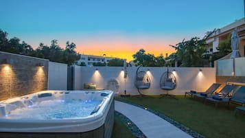 A hot tub, lounge chairs, and a sunset view in a backyard setting.