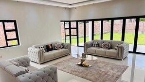 Ein geräumiges Wohnzimmer mit zwei Sofas, einem Couchtisch und großen Fenstern mit Blick auf eine Ziegelwand und Grünflächen.