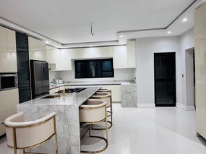 A modern kitchen with a central island, bar stools, and a large refrigerator. - Spacious 5-bedroom house in charming Harare with AC (Harare)