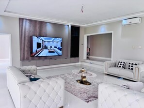 A modern living room with a large flat-screen TV, a round coffee table, and two white sofas. - Spacious 5-bedroom house in charming Harare with AC (Harare)