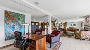 A spacious living area with a wooden desk, comfortable seating, and a large painting on the wall.