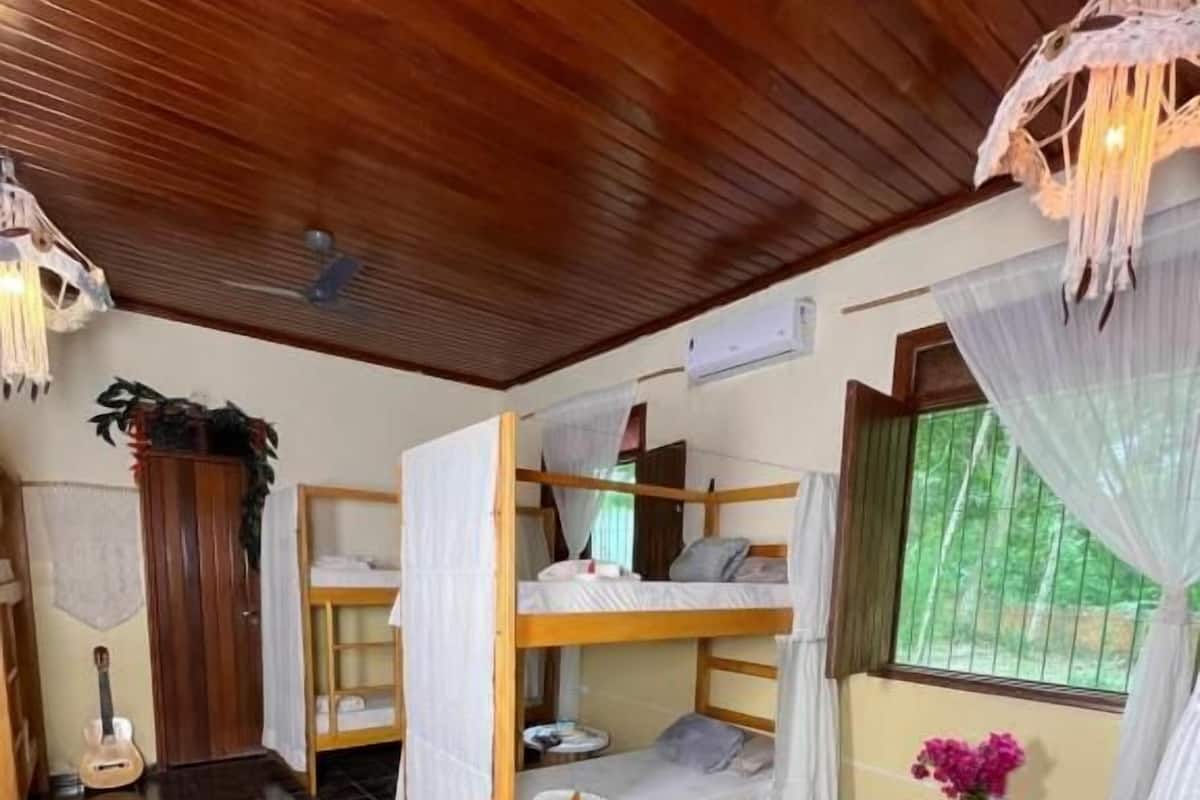 Una habitación con literas, una guitarra, una mesita con un florero y una ventana con cortinas.