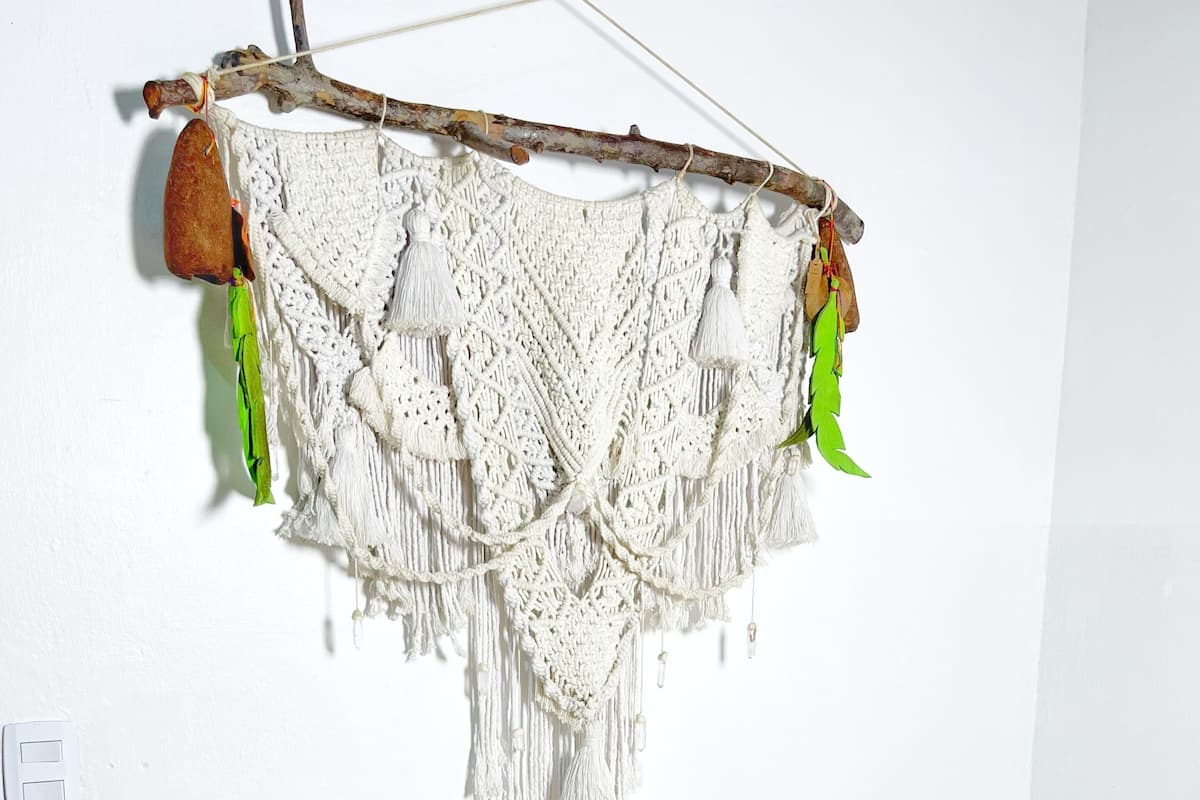 Una cama con dos almohadas y un adorno de macramé en la pared.
