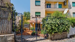 Un immeuble résidentiel doté d’une entrée sécurisée par un portail, d’une antenne parabolique et d’un balcon avec un volet bleu.