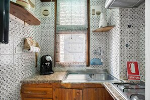 Uma cozinha com azulejos estampados, uma janela com cortinas de renda, uma pia e um fogão.