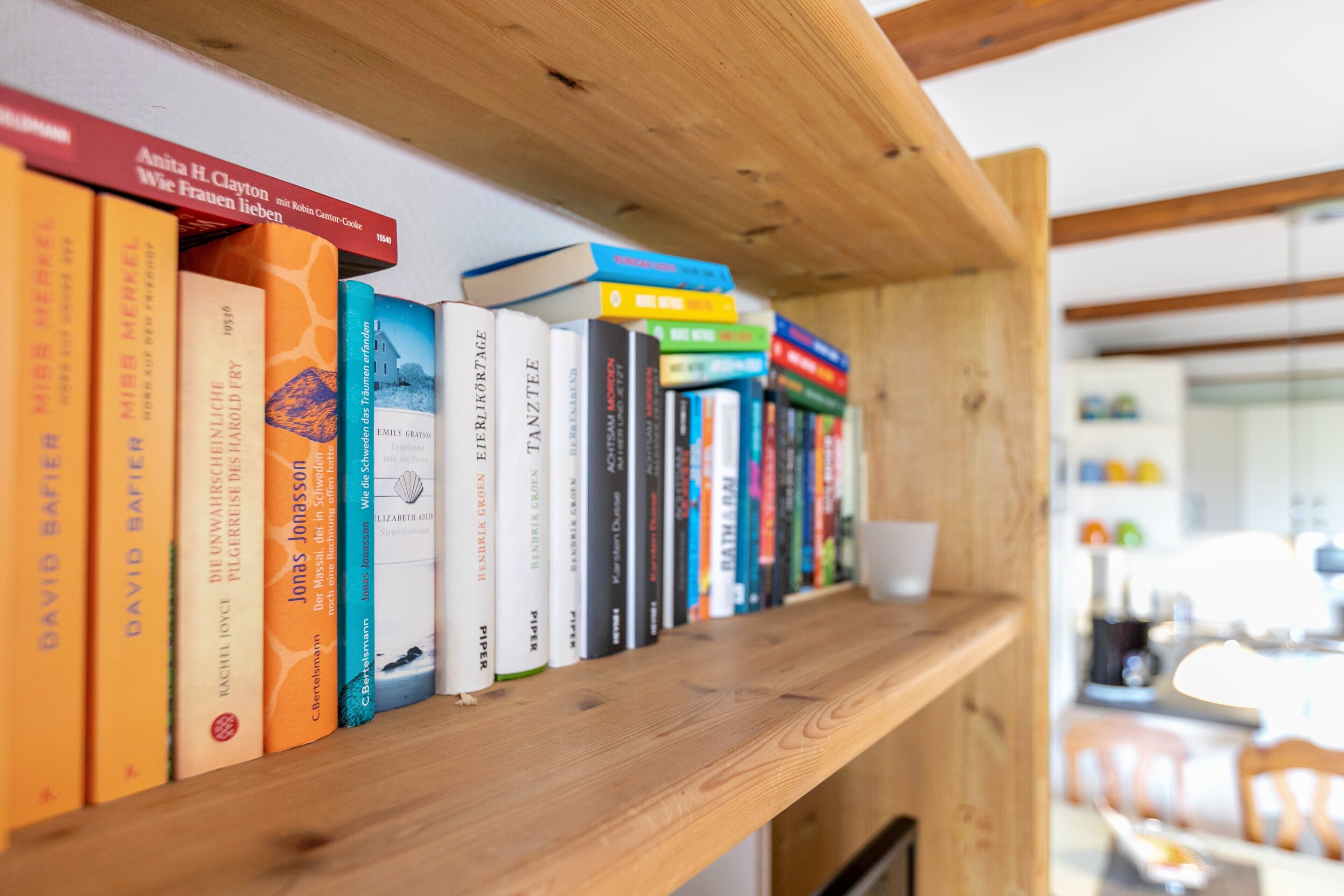 A bookshelf with various books, a wooden shelf, and a cup.