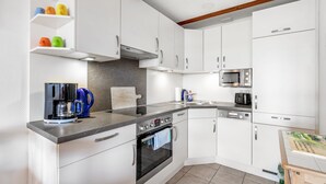 Una cucina moderna con mobili bianchi, forno a microonde integrato, macchina del caffè e piano cottura.